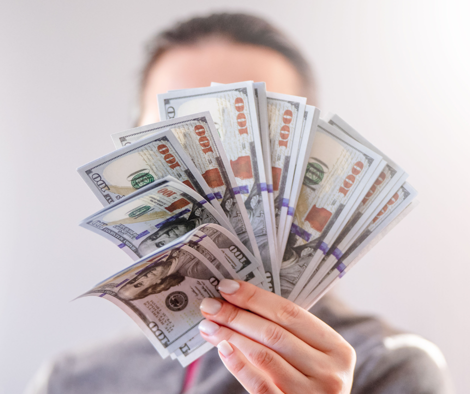 woman's hand holds up fanned out money bills in front of her face
